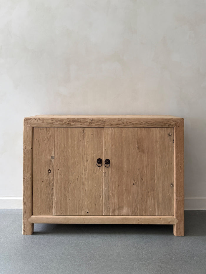 Vintage Reclaimed Elmwood cabinet with two doors on a gray floor and beige limewashed wall. Saffron + Poe