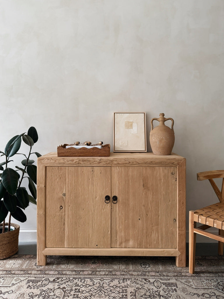 Vintage Reclaimed Elmwood cabinet with two doors styled with art and accessories against a beige limewashed wall. Saffron + Poe