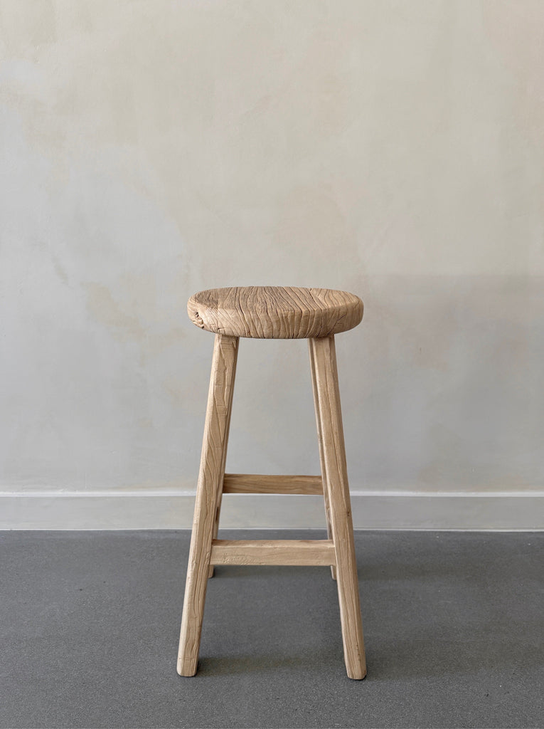 Vintage Reclaimed Elmwood Counter Stool against beige limewashed wall. Saffron + Poe