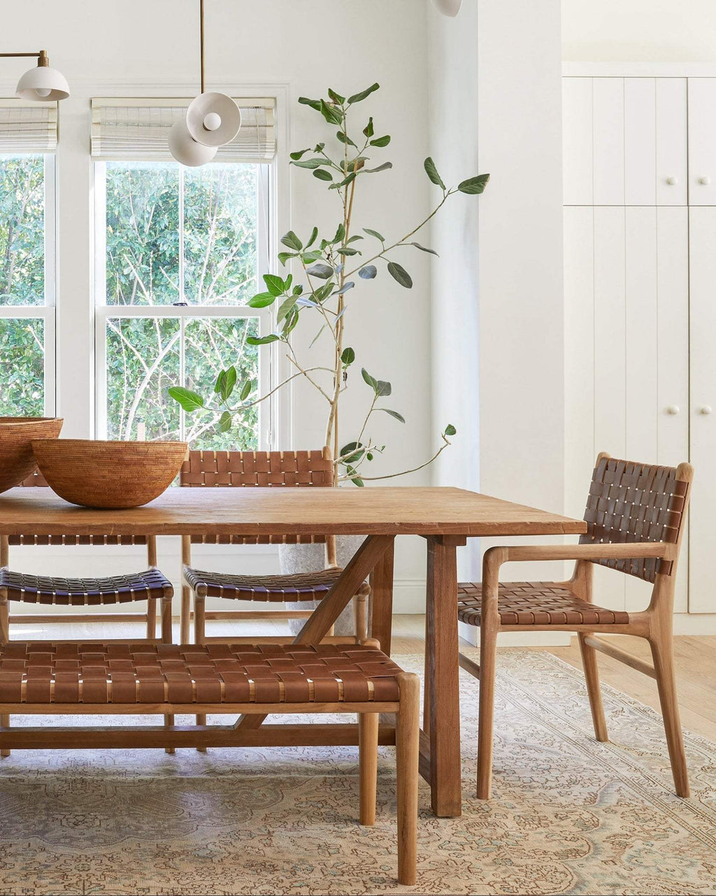 Woven leather bench with teak frame and saddle-colored leather straps in mid-century design in bright dining room