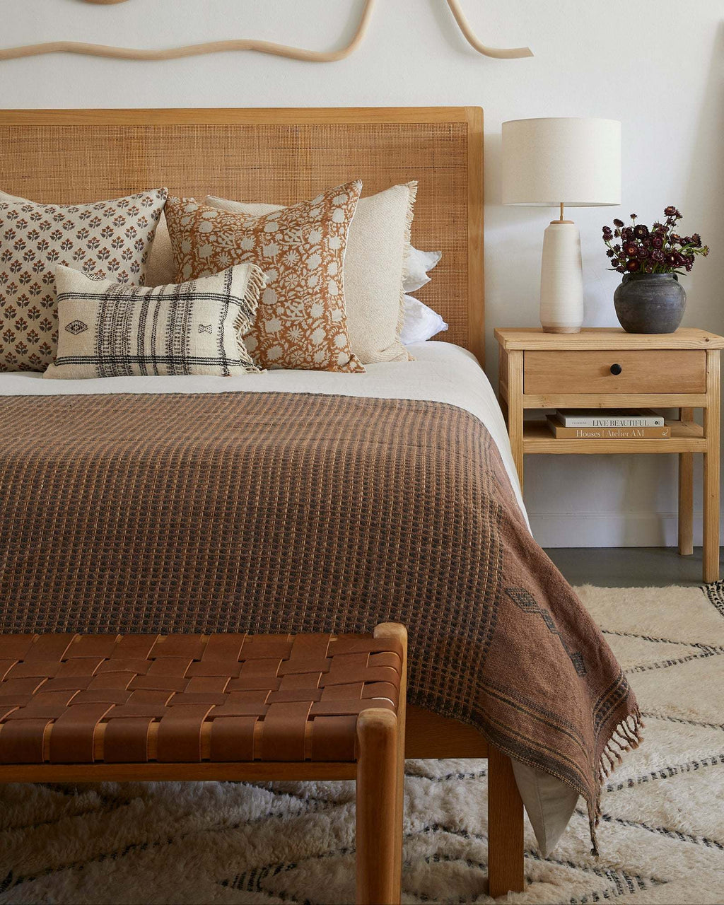 Woven leather bench with teak frame and saddle-colored leather straps in mid-century style at the base of a bed