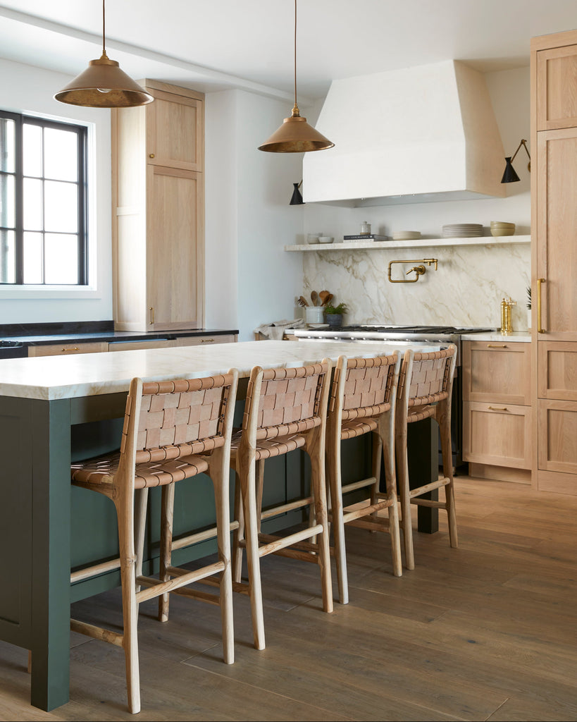 Modern kitchen with wooden cabinets, green island, beige woven leather counter stools, and white countertops