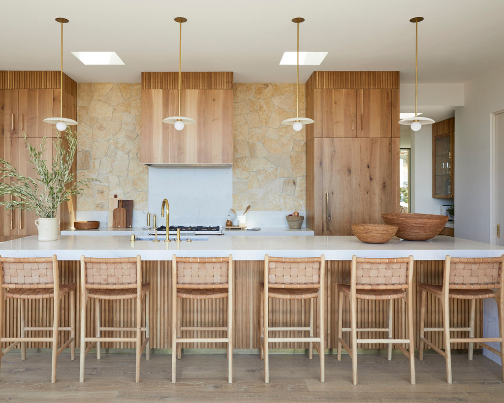 Modern kitchen with beige woven leather counter stools, wooden cabinets, and warm stone backsplash.