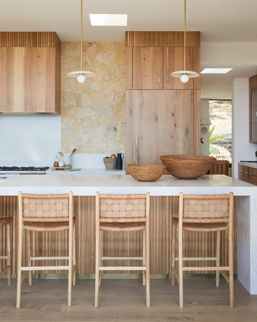 Modern kitchen with wooden cabinets, white countertops, and woven leather counter stools in beige