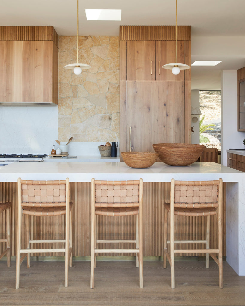 Modern kitchen with wooden cabinets, white countertops, and woven leather counter stools in beige