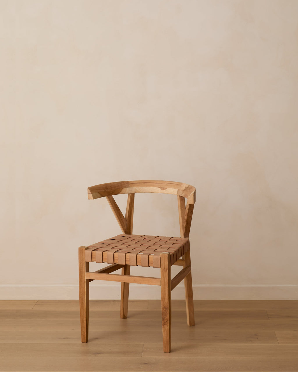 A woven leather wishbone dining chair with a woven seat, positioned against a neutral beige plaster wall and light wood floor.