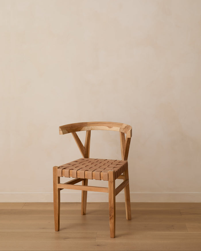 A woven leather wishbone dining chair with a woven seat, positioned against a neutral beige plaster wall and light wood floor.