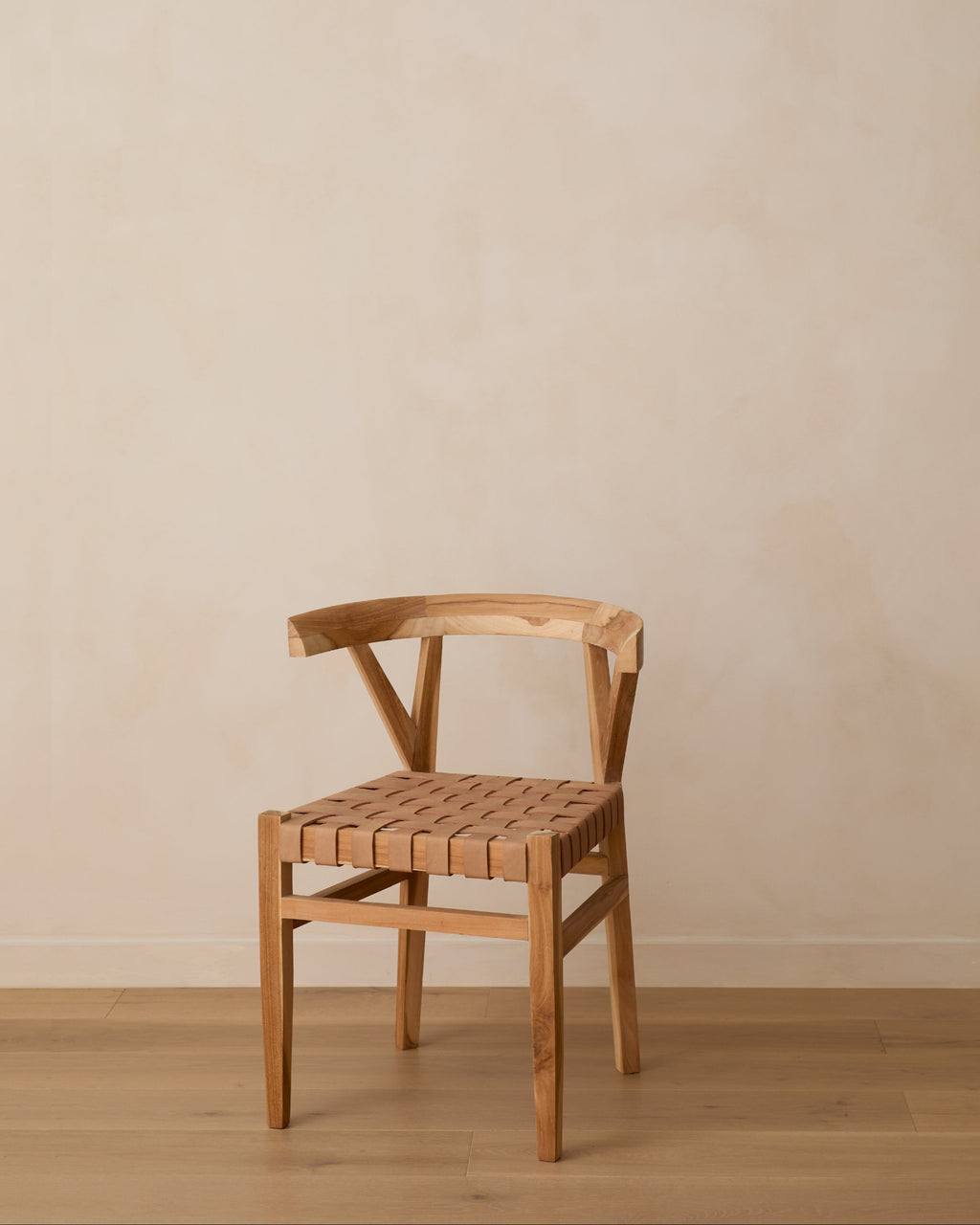 A woven leather wishbone dining chair with a woven seat, positioned against a neutral beige plaster wall and light wood floor.