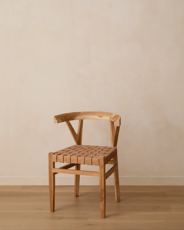 A woven leather wishbone dining chair with a woven seat, positioned against a neutral beige plaster wall and light wood floor.