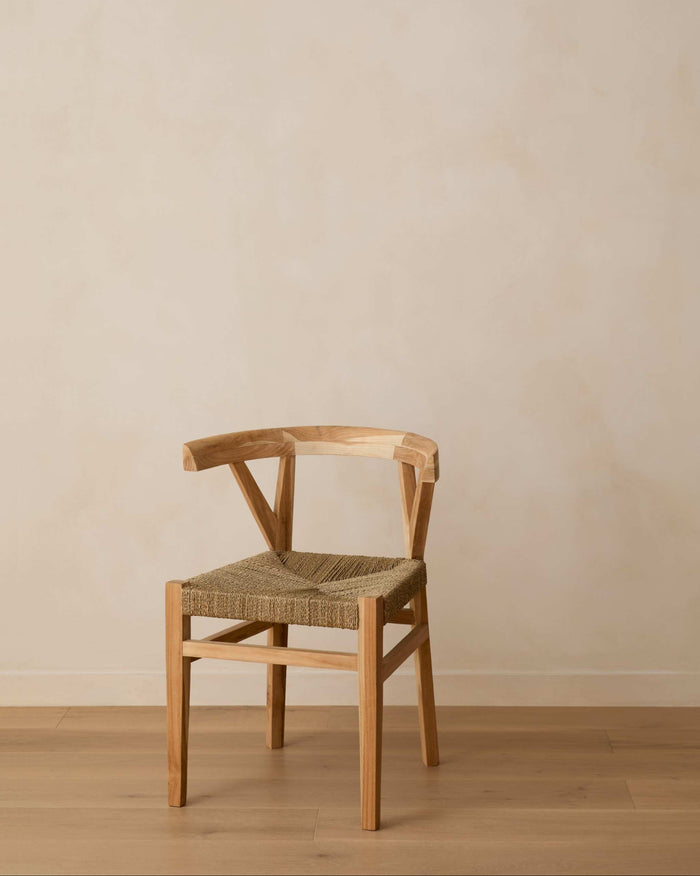 A woven wishbone dining chair with a woven rope seat, positioned against a minimalist beige plaster wall and light wood floor.