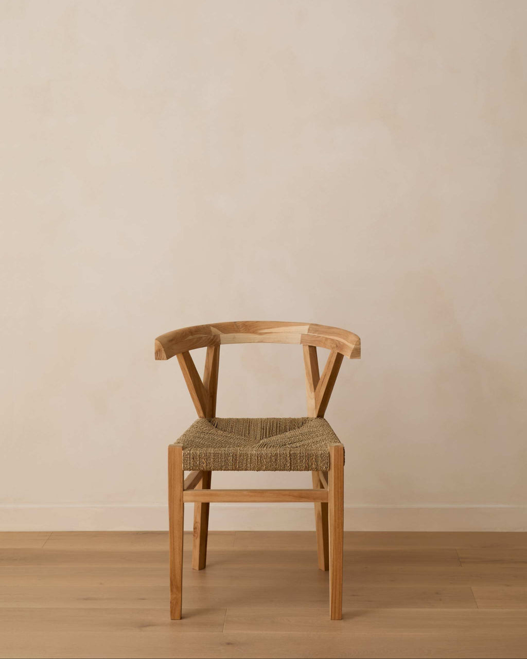 A woven wishbone dining chair with a woven straw seat, positioned against a minimalist beige plaster wall and light wood floor.