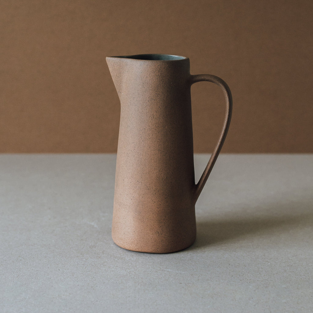 Handcrafted tall ceramic pitcher with earth tone clay textures and glazed interior