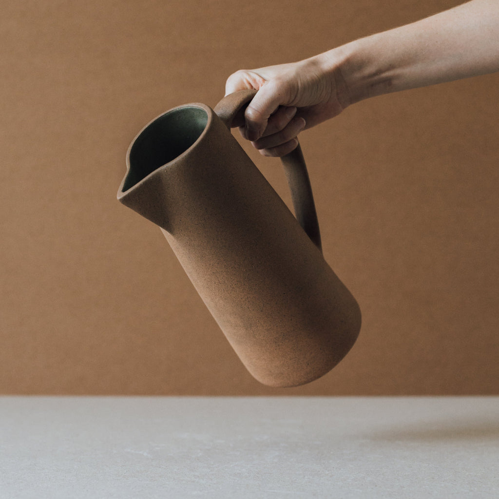 Handcrafted tall ceramic pitcher with natural earth tones and textured clay surface