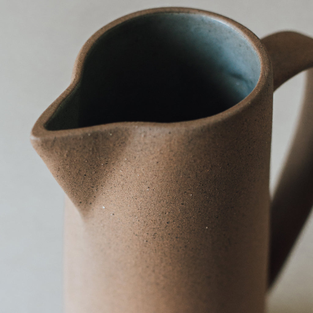 Handcrafted tall ceramic pitcher with natural earth tones and unglazed textured exterior