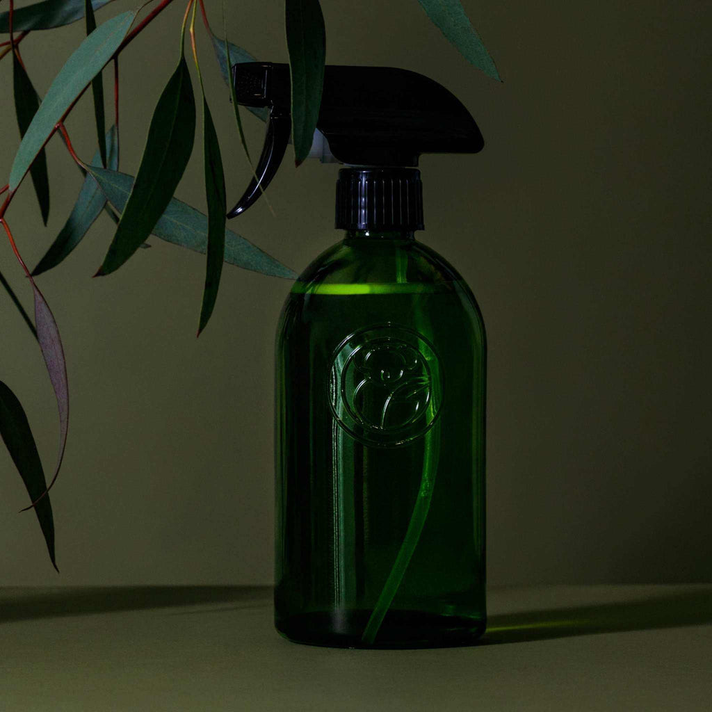 Apothecary Glass Bottle in deep green recycled glass, with a black spray trigger and embossed circular emblem.