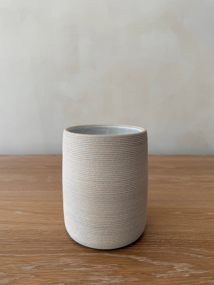 Ivory textured ceramic utensil jar on a wooden surface with a plain background