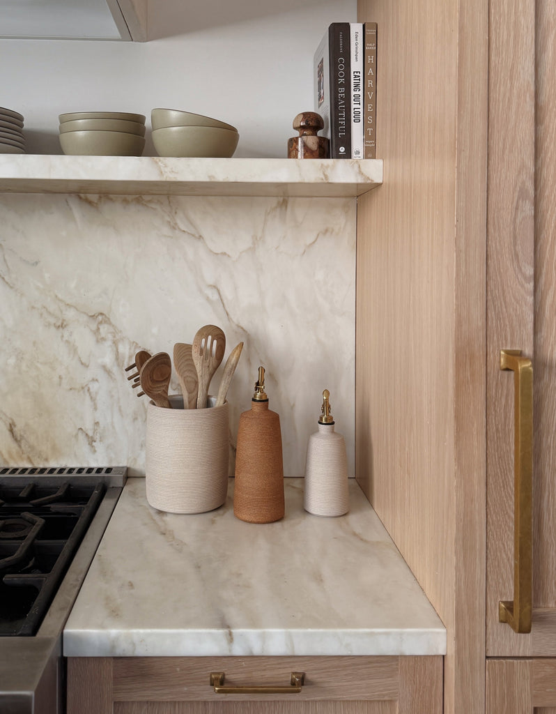 Kitchen counter with marble backsplash, wooden cabinets, and kitchen utensils.