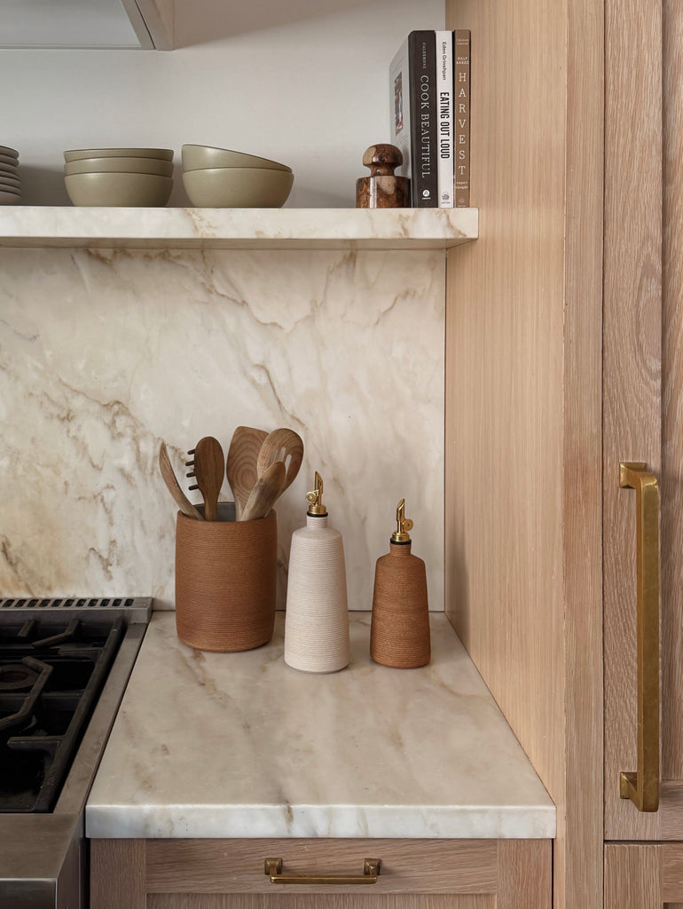Kitchen counter with marble backsplash, wooden cabinets, and kitchen accessories.