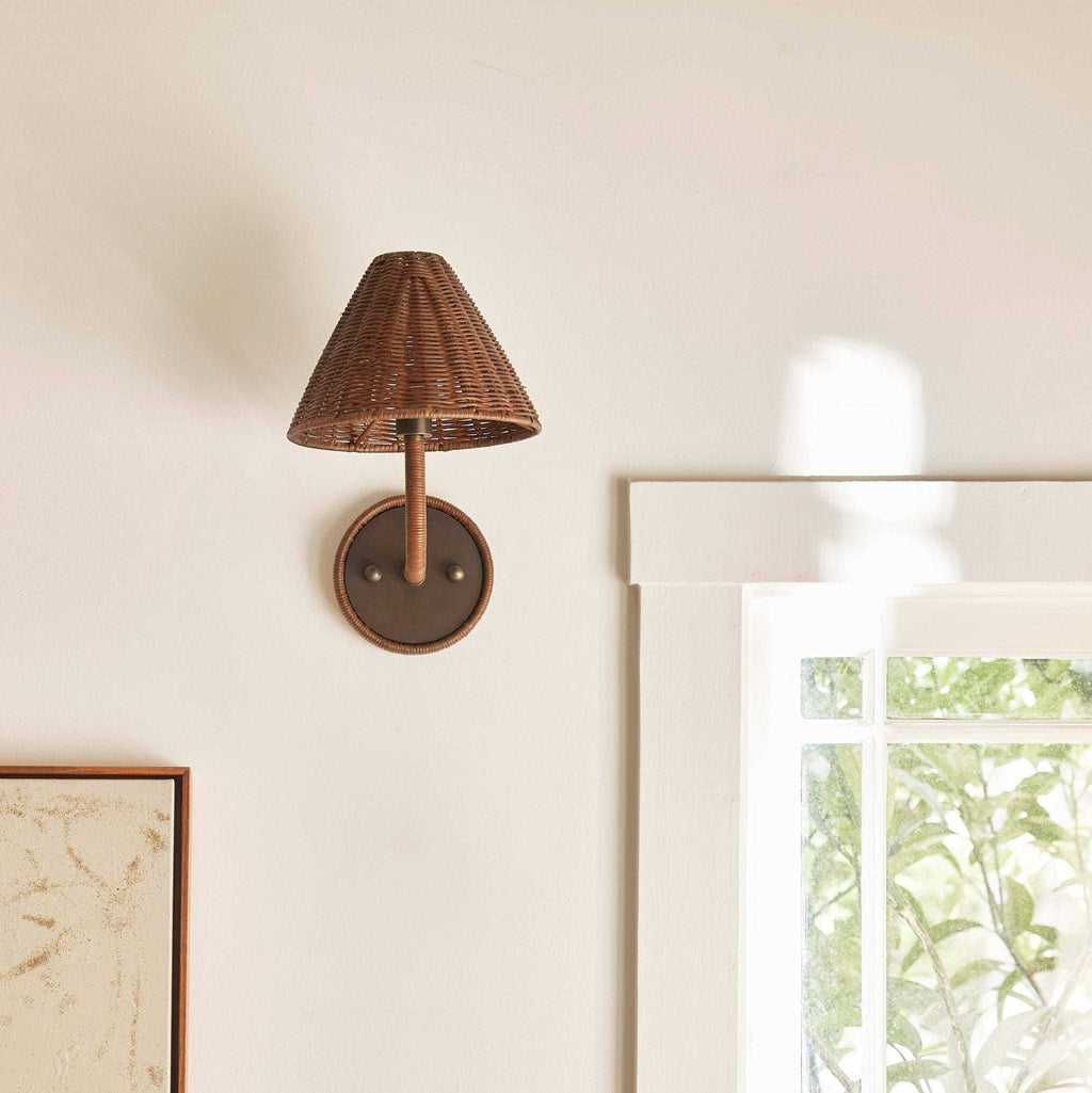 Delphine Wicker Sconce with a dark brown woven tapered shade, slim wicker stem, and round pewter wall plate