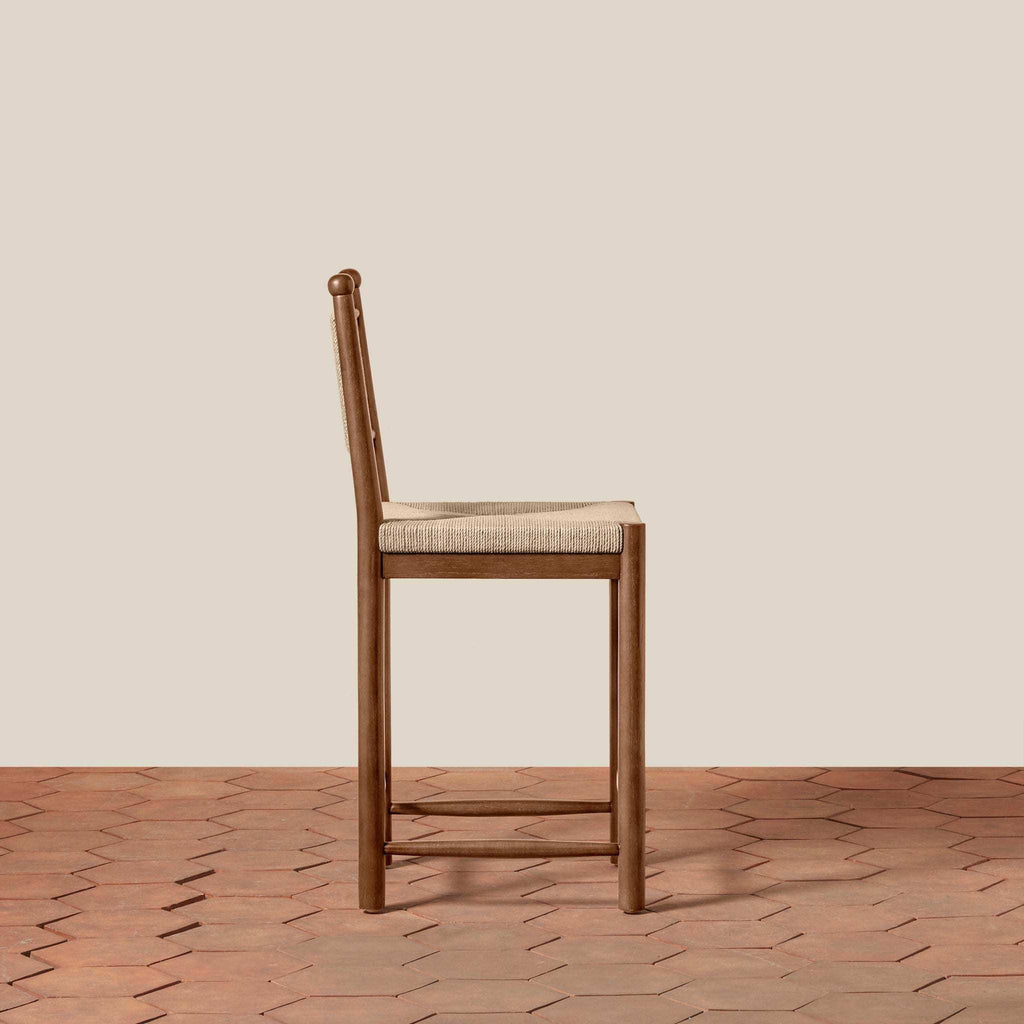 Estela Counter Stool in warm brown wood with a beige woven seat and tall spindle back