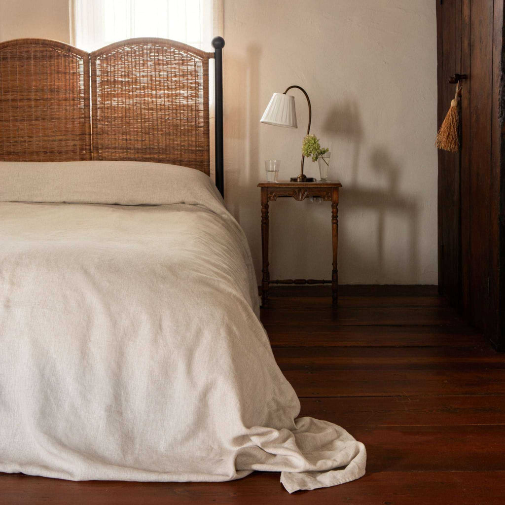 Lacoste Bed with a warm brown woven rattan scalloped headboard, slim black iron posts and neutral bedding