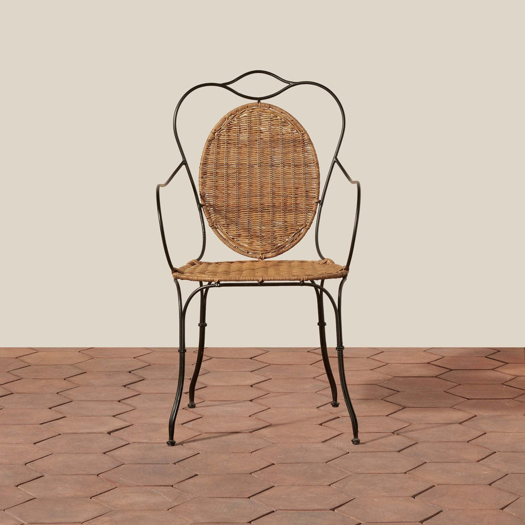 Lacoste Indoor/Outdoor Wicker Arm Chair with natural rattan seat and backrest, black wrought iron frame featuring elegant curved arms and legs
