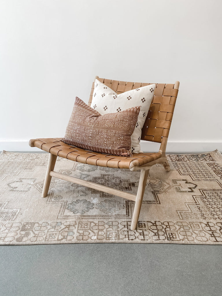 Styled view of Woven Leather Strap Lounge Chair in Beige against white background on vintage Turkish oushak rug with pillows. Teak wood and leather straps. Handcrafted in Bali. - Saffron and Poe