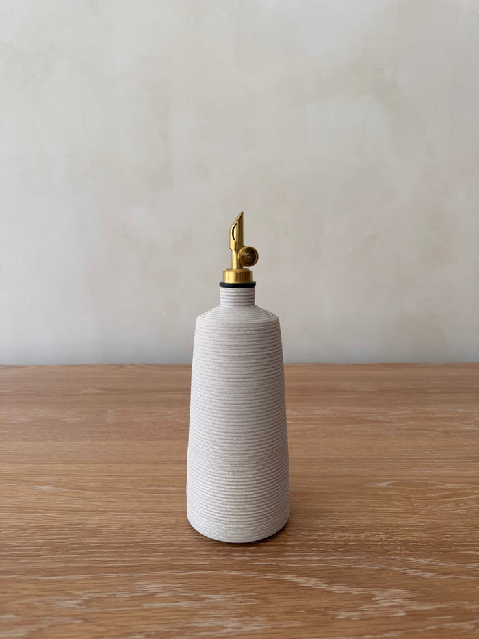 White ceramic olive oil dispenser with brass nozzle on a wooden surface
