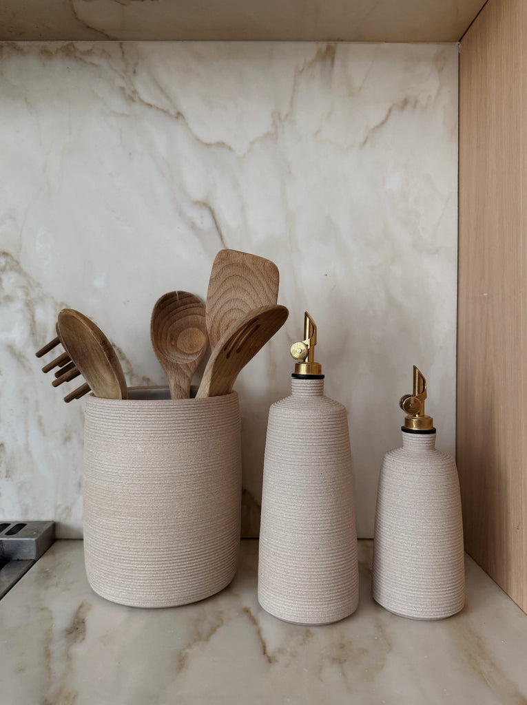 Olive oil bottle with balsamic vinegar bottle and utensil jar with wooden spoons on a marble countertop