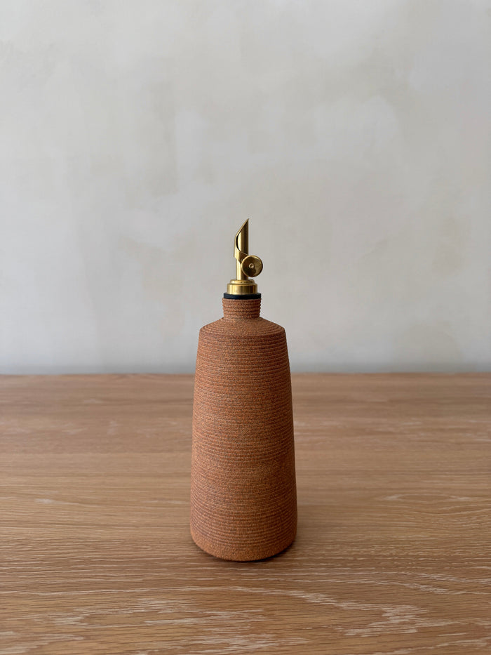 Terracotta ceramic olive oil dispenser with brass cap on a wooden surface