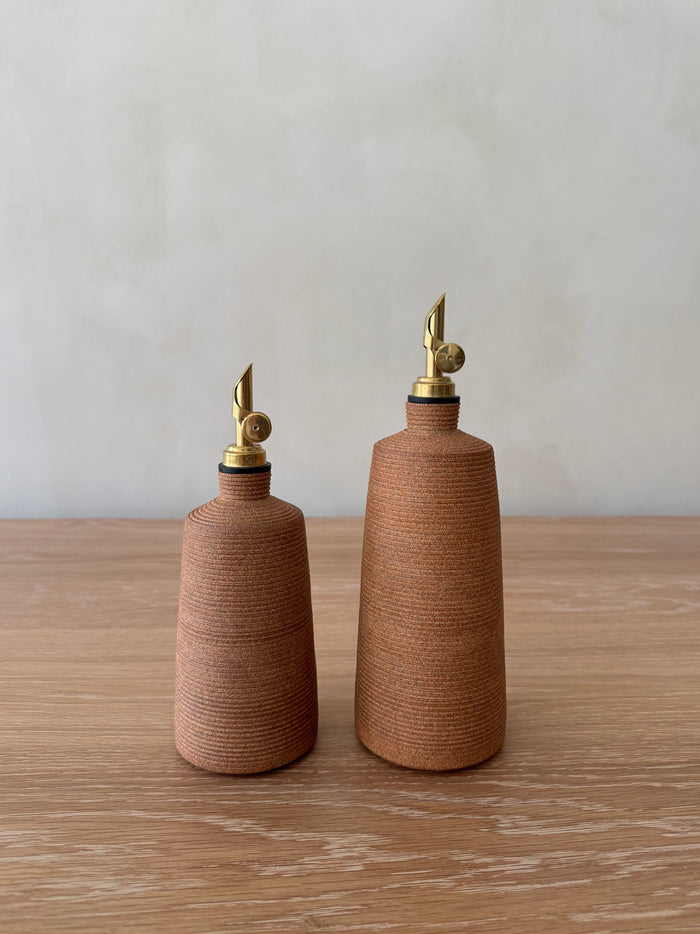 Terracotta ceramic oil dispensers with brass nozzles on a wooden surface.