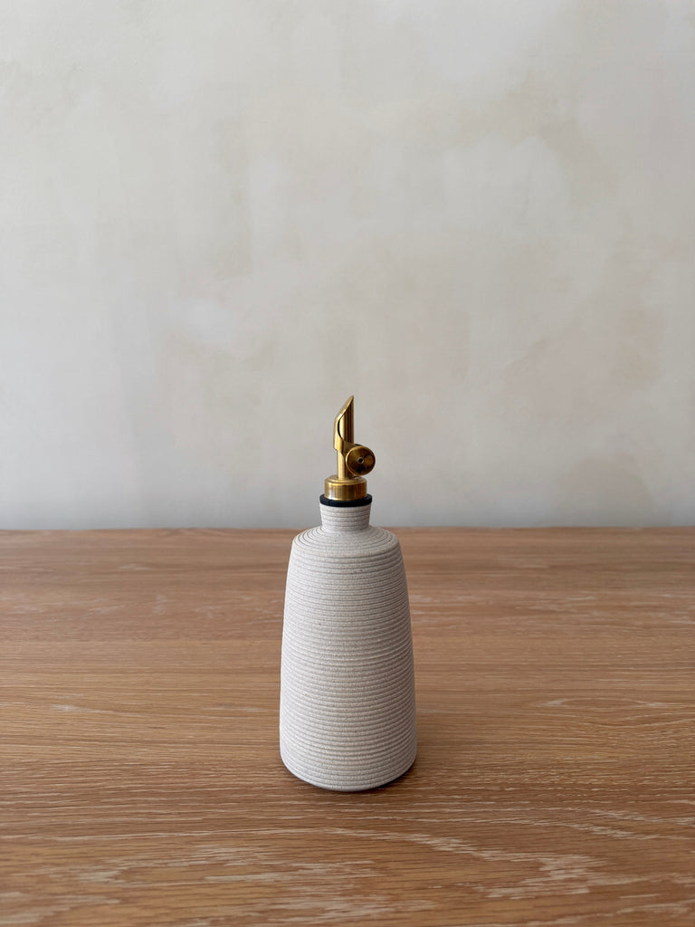 White ceramic vinegar bottle with brass nozzle on a wooden surface