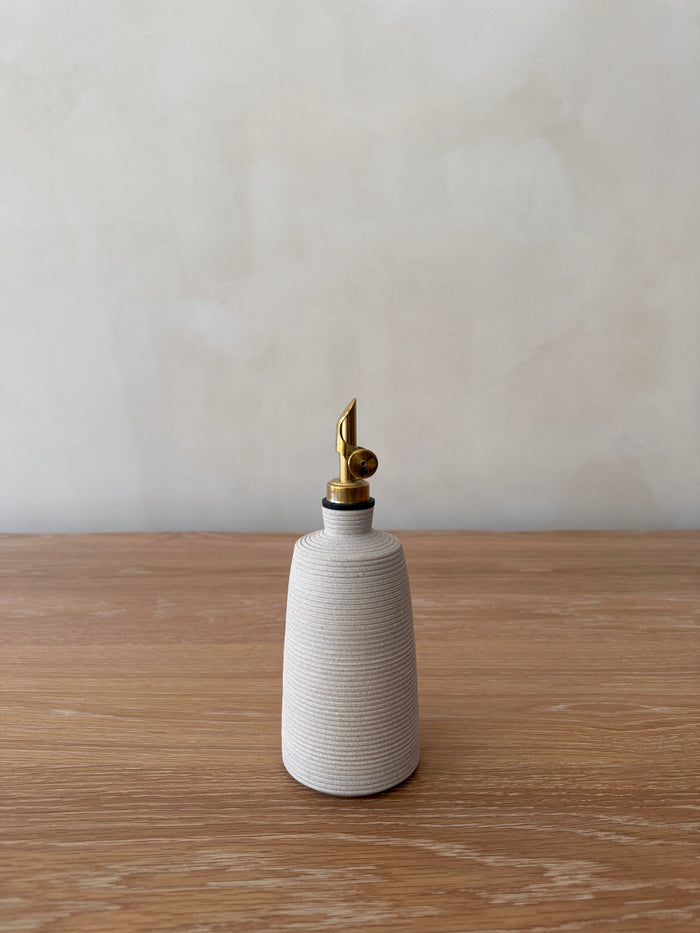 White ceramic oil dispenser with brass nozzle on a wooden surface