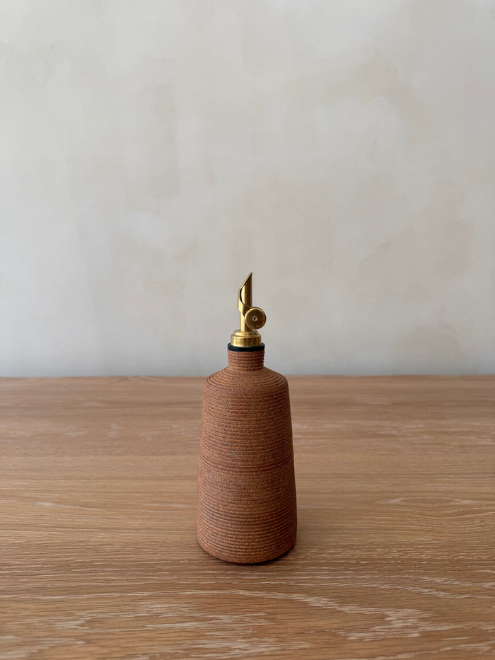 Terracotta ceramic oil bottle with brass cap on a wooden surface