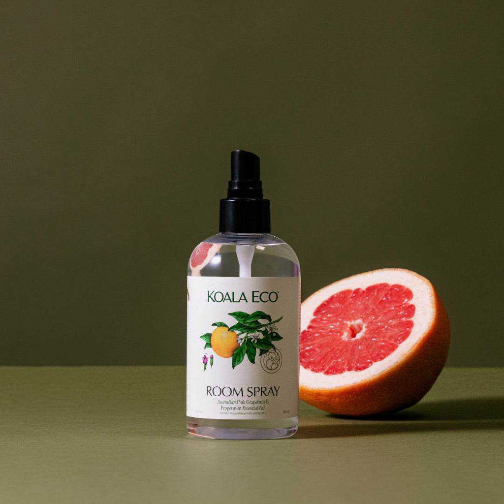 Pink Grapefruit + Peppermint Room Spray in a clear bottle with a black pump and botanical label, beside a halved grapefruit