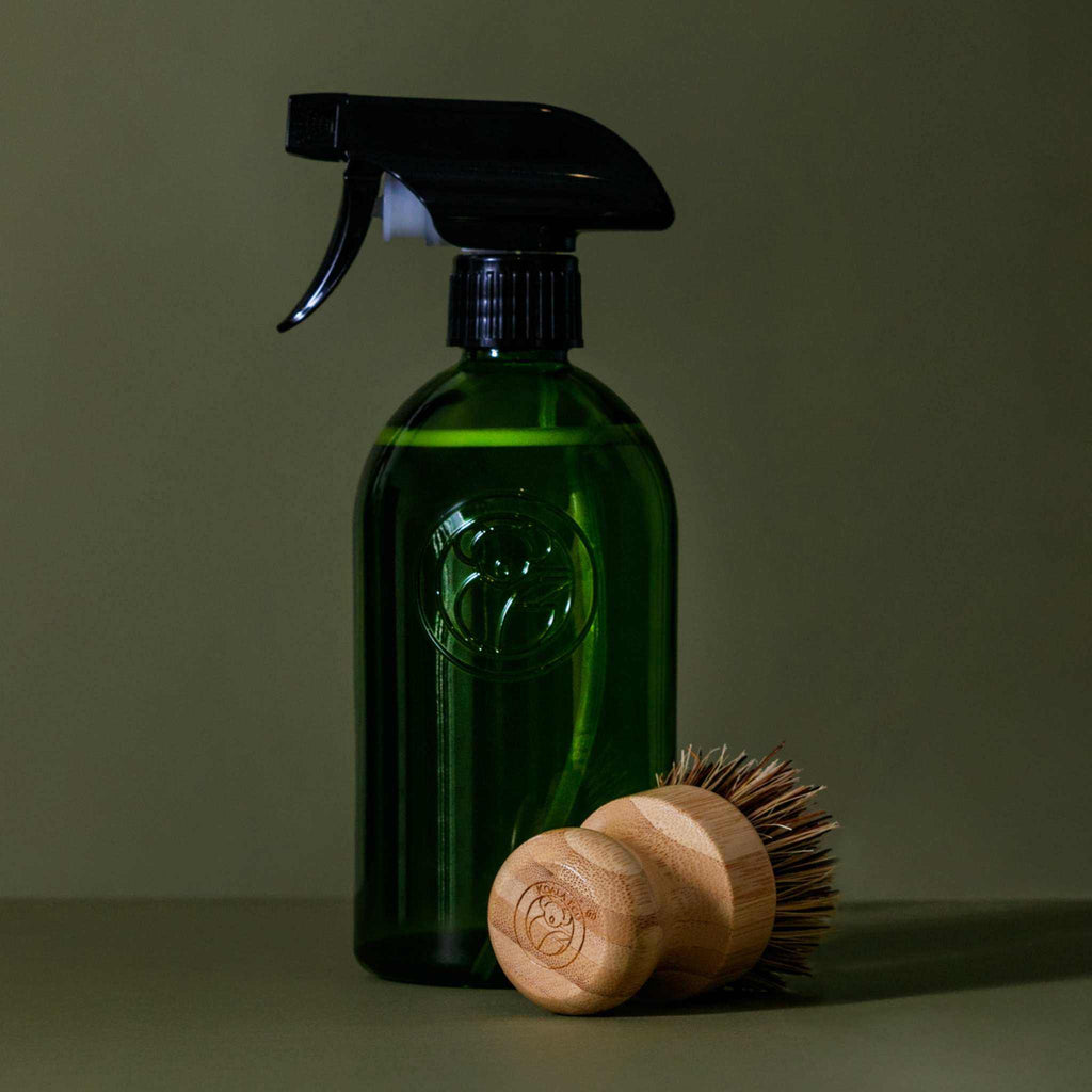 Scrubbing Brush with a round light bamboo base and dark sisal bristles, shown beside a green spray bottle