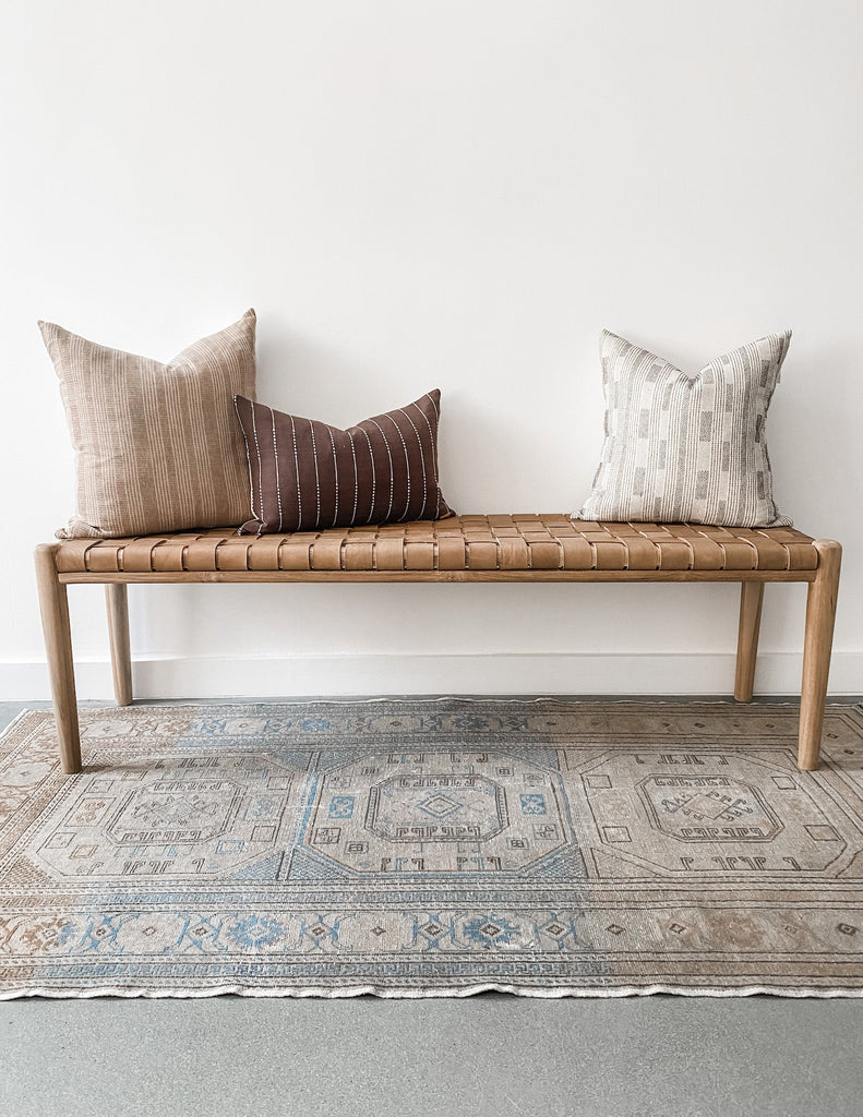 Styled 60" woven leather strap bench in beige with vintage Turkish oushak rug and three pillows. Handcrafted in Bali. - Saffron and Poe