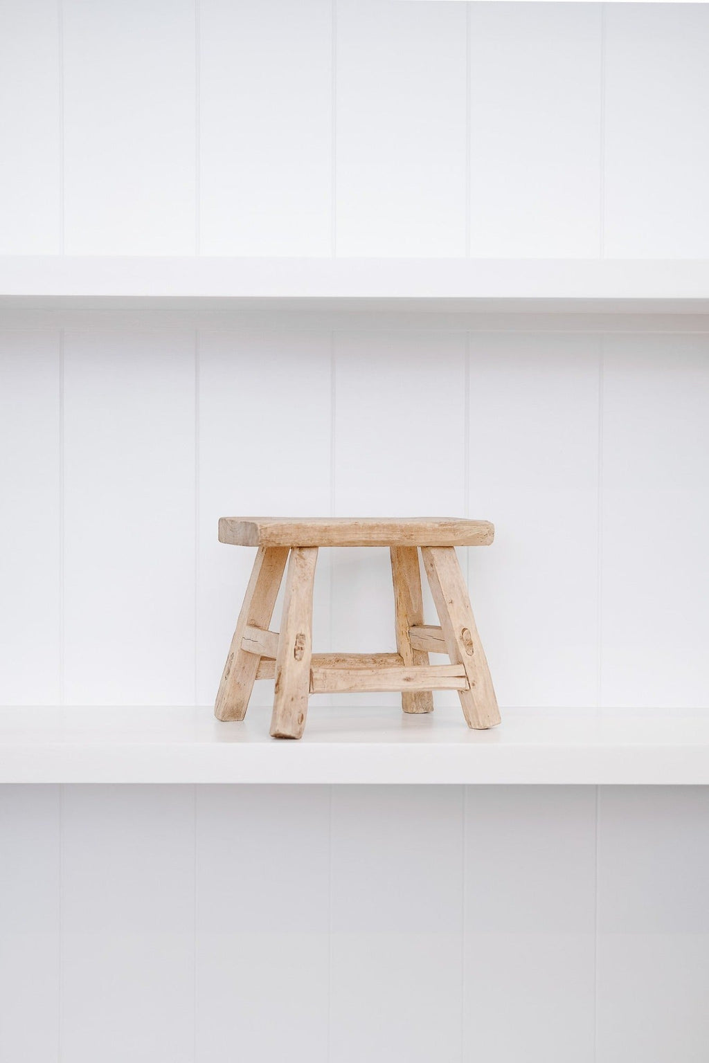 Petite antique elmwood stool with mortise and tenon joinery on white shelf