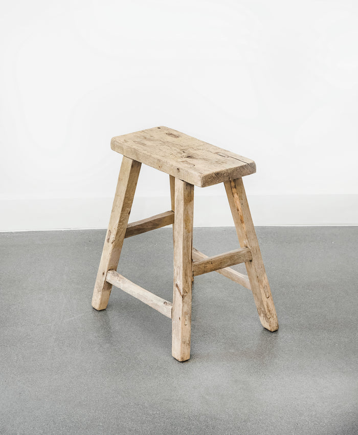 Angled view of vintage rectangular stool on concrete floor with white walls. - Saffron and Poe