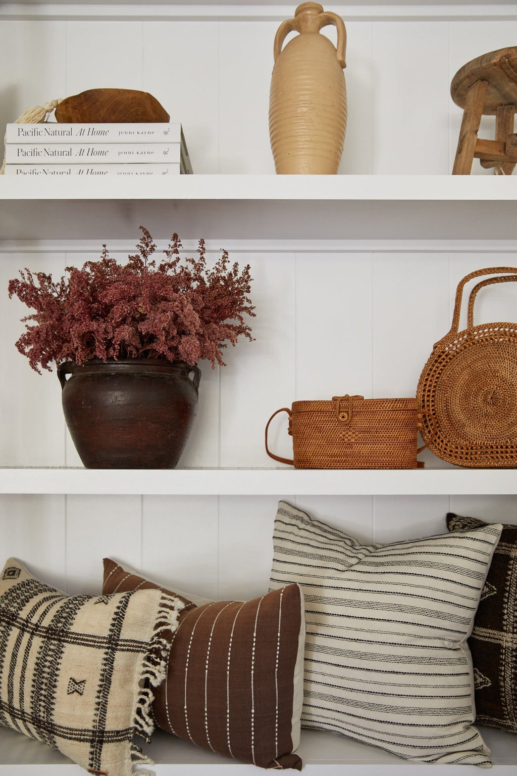 Antique clay pot with dried flowers on white shelf styled with woven baskets and pillows