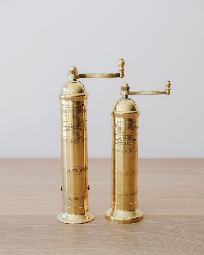 Front view of Atlas Brass Salt and Pepper Grinders - 8", 9" on an oak table against a white wall.