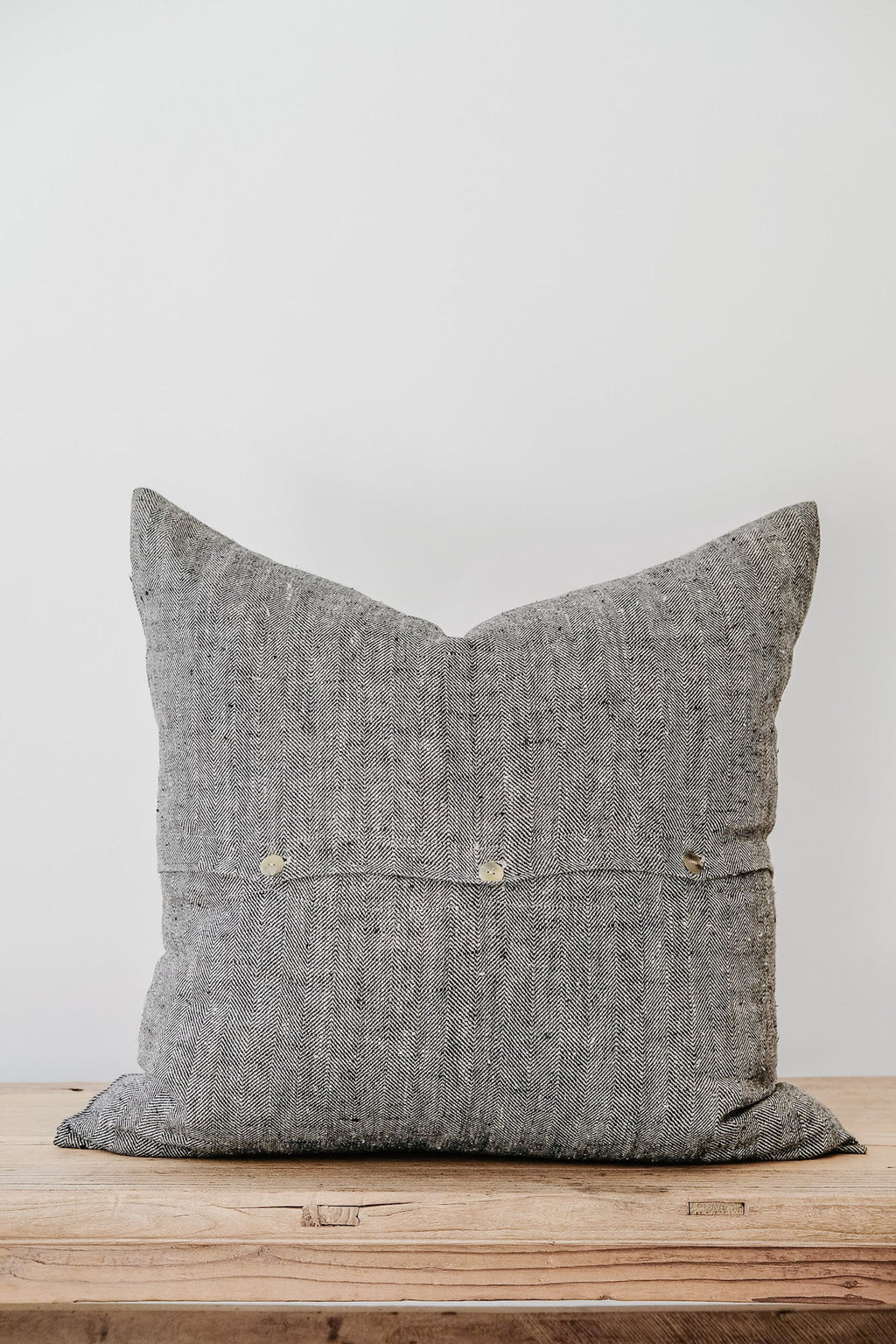 Charcoal chevron linen pillow with textured fabric on wooden surface against white wall