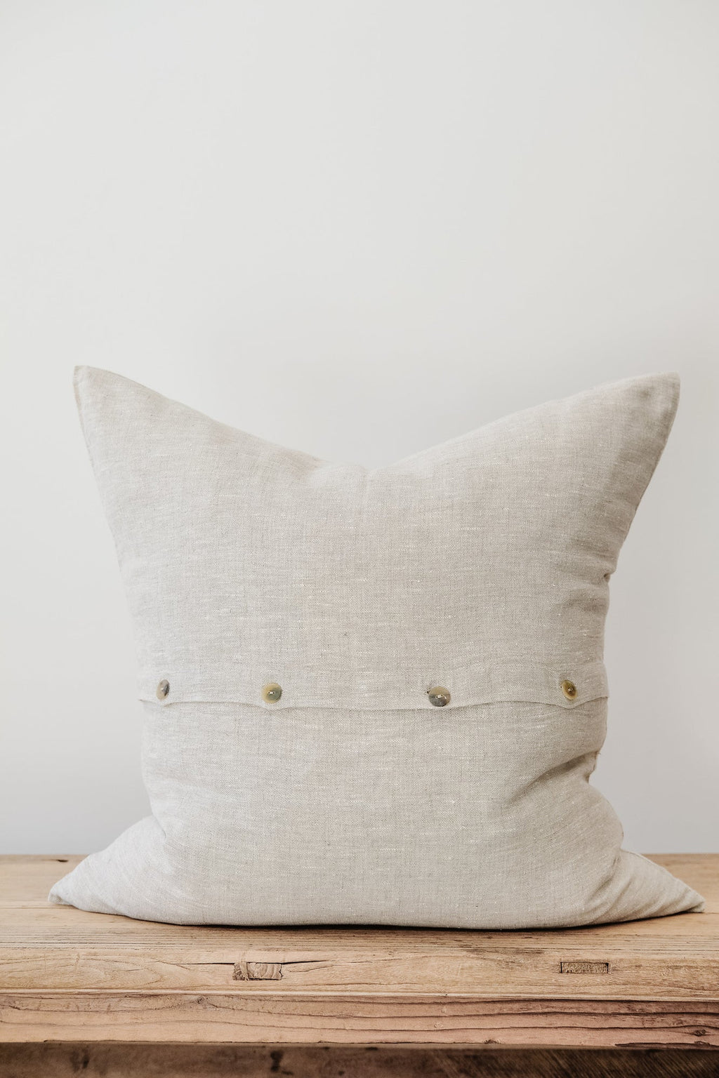 Natural linen pillow with neutral color and button details on wooden surface