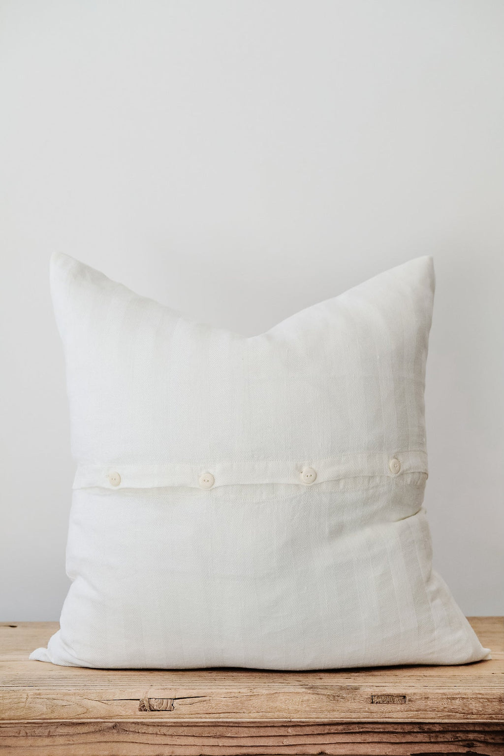 White chevron linen pillow with button detail on wooden surface against white background