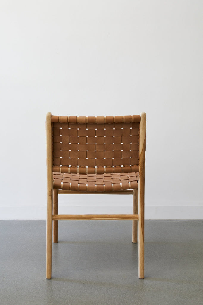 Back view of the Woven Leather Strap Dining Arm Chair in Beige against a white background and concrete floors. - Saffron and Poe
