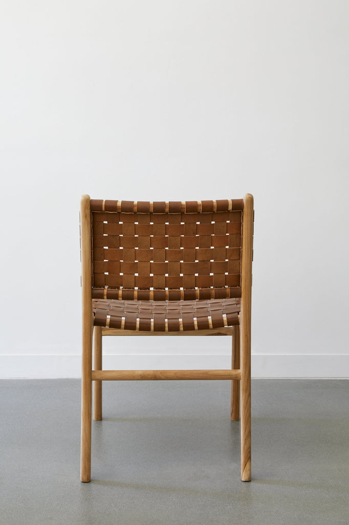 Back view of the woven leather strap dining arm chair in saddle against white background and concrete floors. - Saffron and Poe