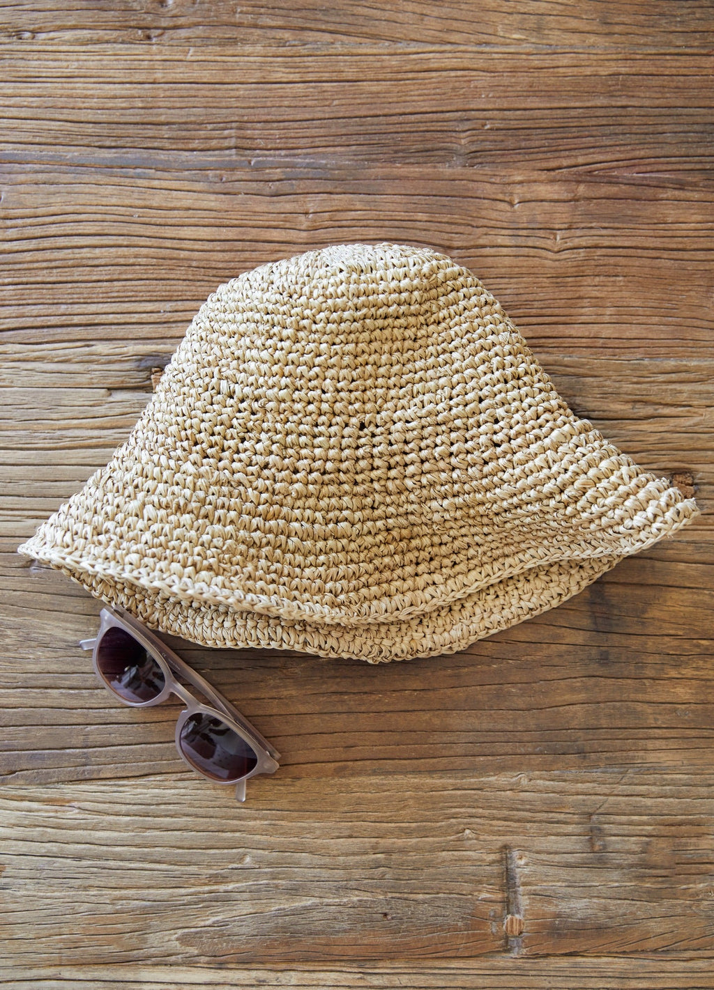 Handwoven Balinese bucket hat made from natural water hyacinth placed on wooden surface with sunglasses