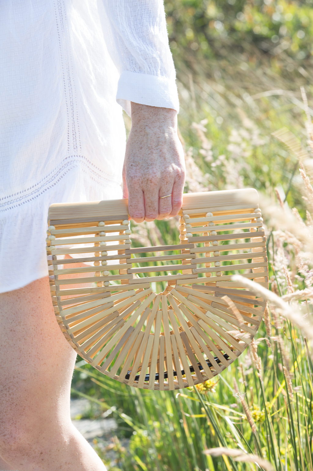 Hand holding Bamboo Crescent Clutch made from natural bamboo in outdoor setting