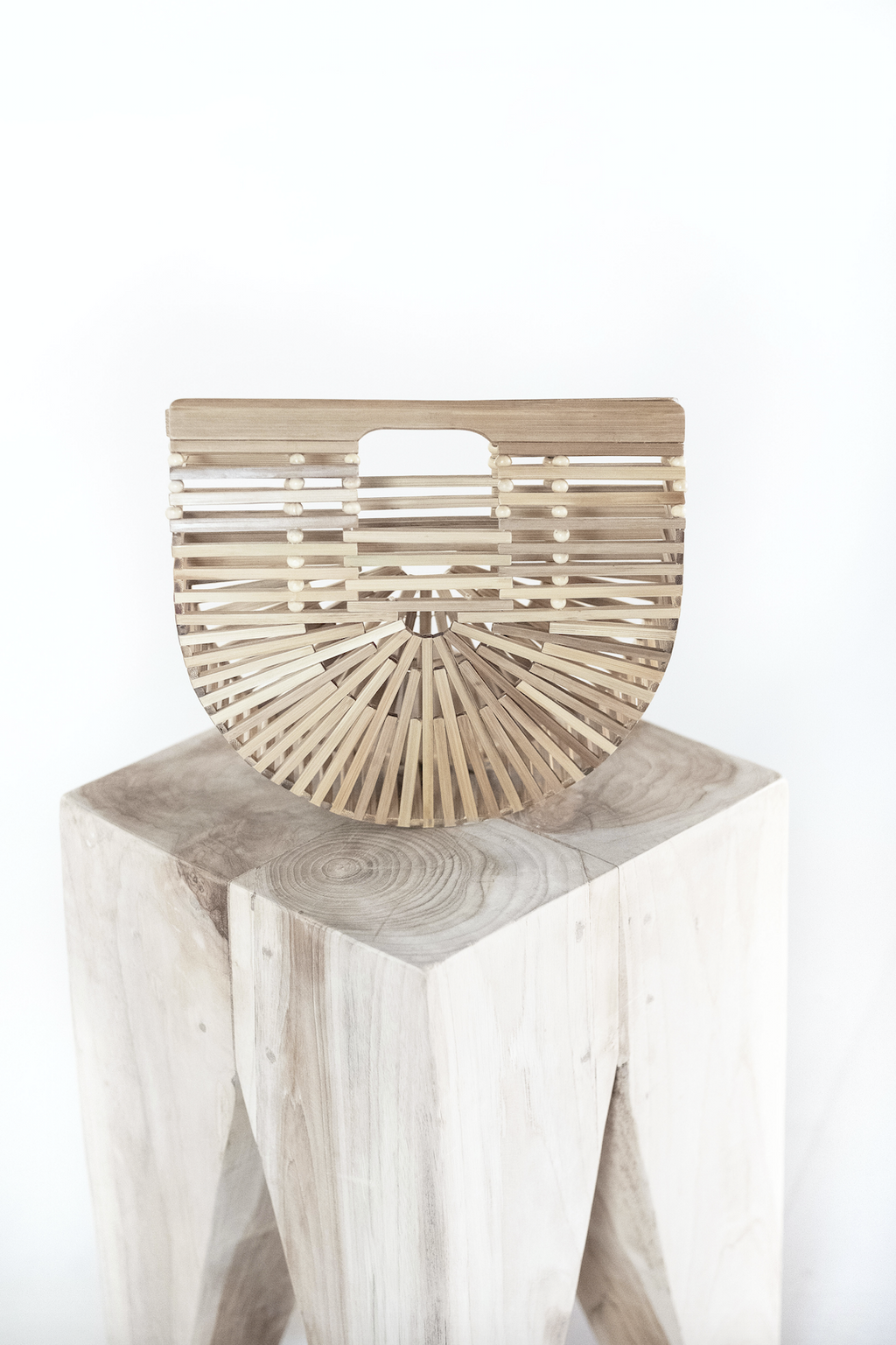 Bamboo Crescent Clutch with geometric pattern handcrafted from natural bamboo on wooden stool