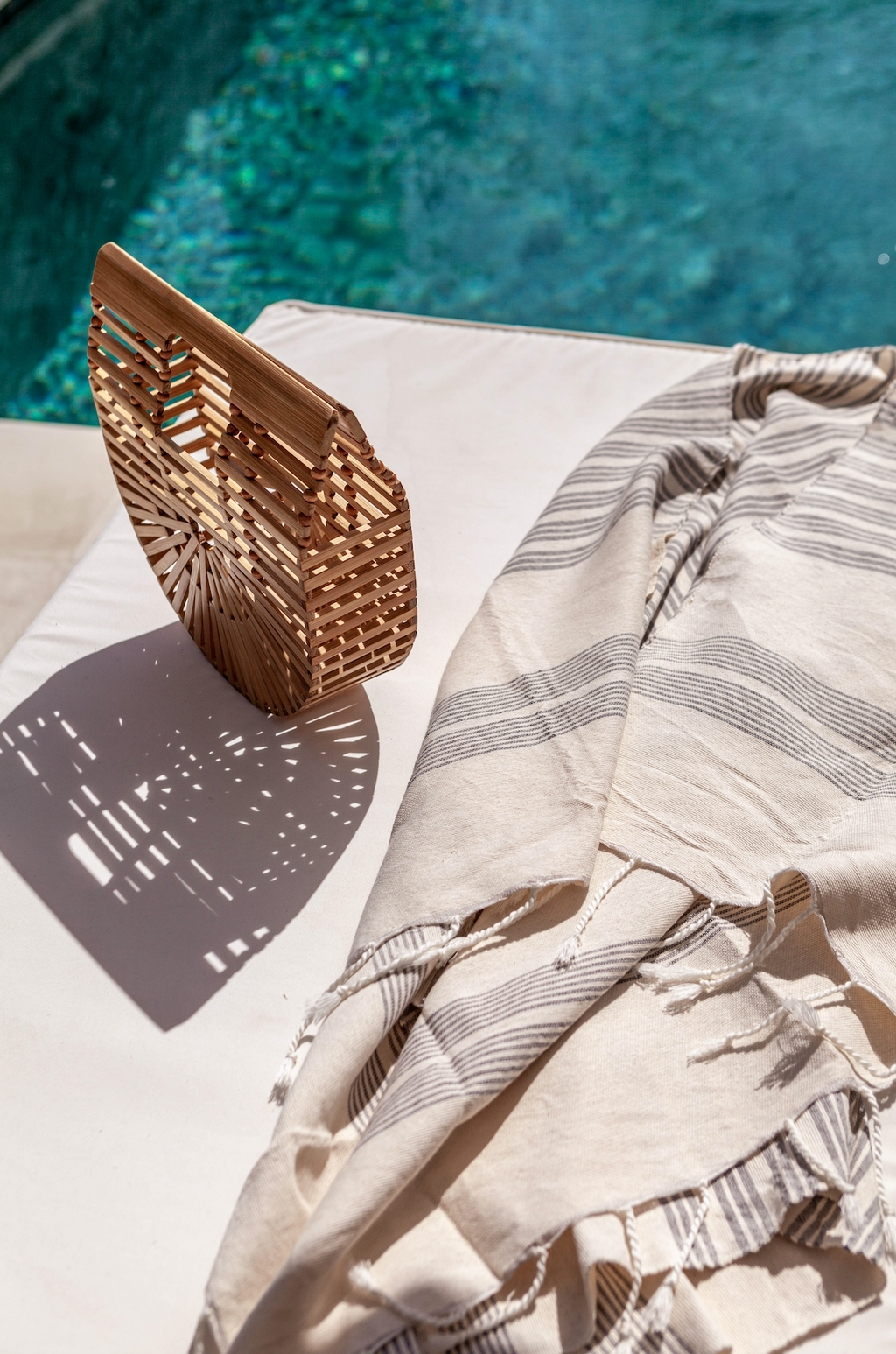 Bamboo Crescent Clutch with geometric pattern resting on sunlit poolside lounge chair next to striped towel